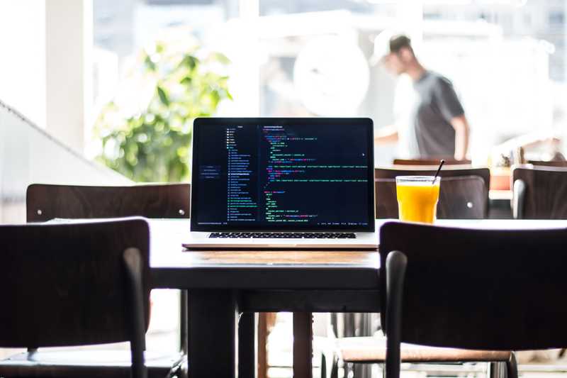 MacBook Pro with code on the screen sitting on a wooden table with two chairs